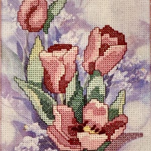 May include: Cross-stitch artwork featuring a bouquet of pink and red tulips with green leaves. The needlepoint design is set against a soft, lavender background, creating a vintage floral aesthetic.