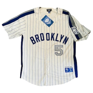 May include: White baseball jersey with blue and grey stripes. The jersey has "BROOKLYN" in blue lettering on the front and the number "5" in grey lettering. The jersey has a tag that says "ROYAL GIANTS" on the right sleeve.