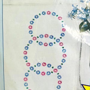 Puede incluir: Un panel de tela blanco con un diseño de bordado a mano de tres círculos concéntricos de flores rosas y azules. El texto "For Hand Embroidery" está impreso en la esquina superior izquierda. El texto "Crafted with Pride in U.S.A." está impreso en la esquina inferior izquierda.
