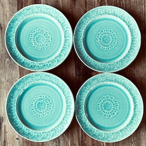 Puede incluir: Cuatro platos de cerámica turquesa con un detallado diseño floral en el borde y un diseño circular central. Los platos están dispuestos sobre una superficie de madera, mostrando su color y textura.