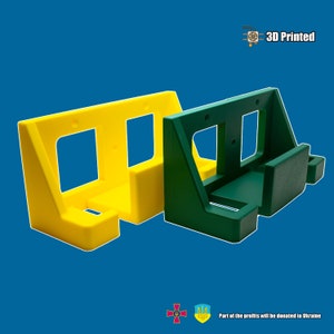 May include: Two 3D printed wall mounts, one yellow and one green. The mounts are designed to hold items on a wall. The text "3D Printed" is visible in the image.