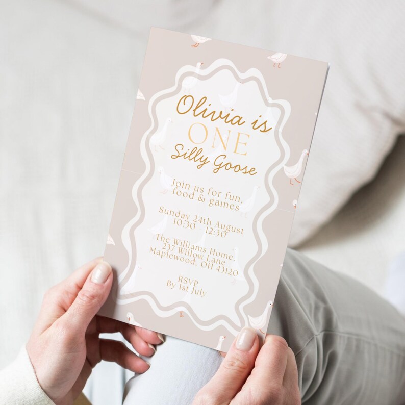 May include: A beige invitation card with gold text and a wavy border. The text reads "Olivia is ONE Silly Goose" with event details. Small goose illustrations are scattered around the border. The card is held by a person.