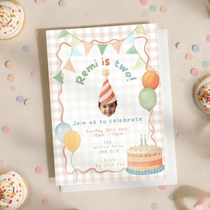 以下が含まれることがあります： 「Remi is two!」のテキストが入った誕生日招待状には、パーティーハットをかぶった子供の写真が掲載されています。招待状には、風船、ケーキ、RSVPの日付など、パーティーの詳細が含まれています。