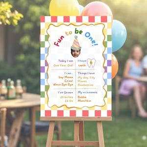 Puede incluir: Un colorido letrero de cumpleaños sobre un caballete con el texto "Fun to be One!" y una foto de un bebé con un gorro de fiesta. El letrero incluye detalles sobre el niño, incluyendo una altura de 73,66 cm y un peso de 9,98 kg.