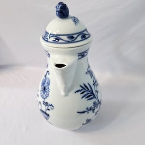 Puede incluir: Tetera de cerámica blanca con diseños florales y de hojas azules. La tetera tiene un pico curvo, una tapa con un pomo azul y un asa. El diseño es de estilo clásico azul y blanco, ideal para servir té.