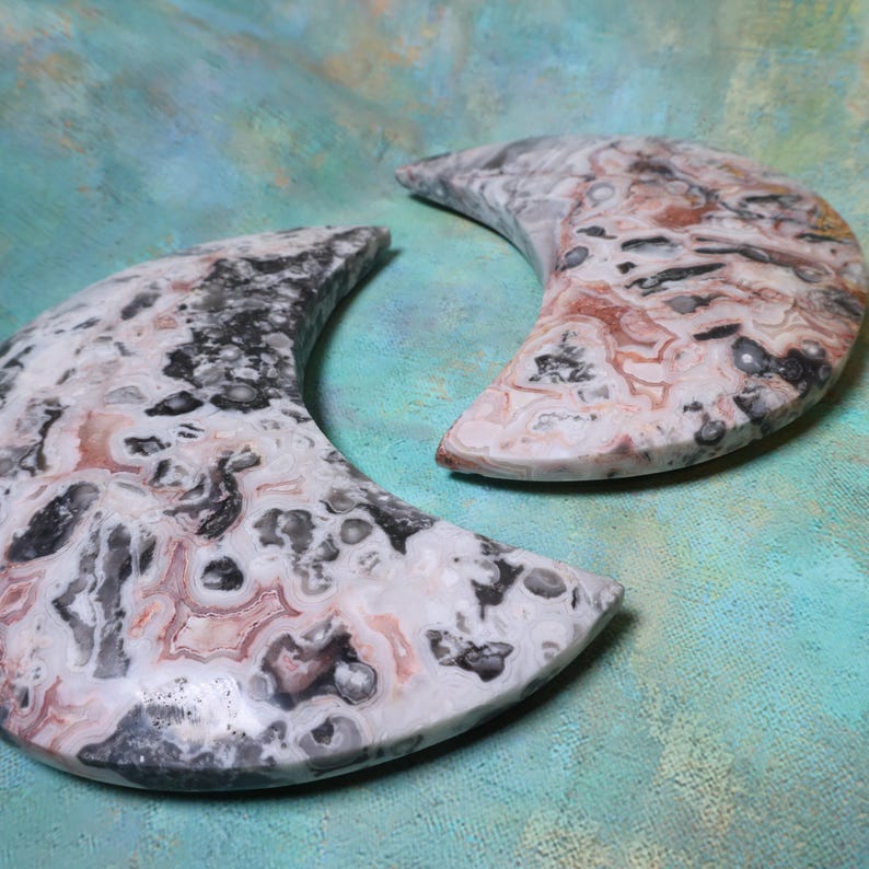 Puede incluir: Dos objetos decorativos en forma de media luna. Los objetos est&aacute;n hechos de un material de piedra con una mezcla de colores, incluyendo blanco, negro y marr&oacute;n rojizo. La piedra tiene un aspecto estampado. El fondo es de color verde azulado.