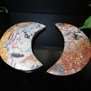 Puede incluir: Dos piedras en forma de media luna con un patr&oacute;n veteado. Las piedras presentan una mezcla de colores, incluyendo blanco, amarillo, rojo y gris. Las superficies pulidas reflejan la luz, resaltando las variaciones naturales de la piedra.