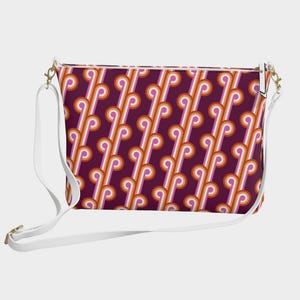 May include: A rectangular crossbody bag with a white strap and gold-coloured hardware. The bag features a repeating pattern of orange, white, and pink curved lines on a dark purple background. The bag is designed for carrying essentials.
