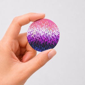 May include: A circular disc featuring a vibrant gradient pattern that transitions from pink at the top to white, purple, and deep blue at the bottom. The design consists of repeating, swirling, flame-like shapes that create a fluid, marbled effect.