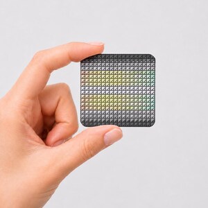 May include: A small square tile featuring a repeating geometric pattern of tiny triangles. The design displays a gradient effect, transitioning from dark gray at the top and bottom edges to lighter shades of yellow, green, and white in the center.