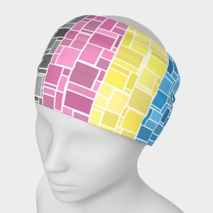 May include: A colourful headband featuring a geometric pattern of squares in shades of grey, pink, yellow, and blue. The headband is made of a soft, stretchy material and is designed to fit comfortably around the head. Suitable for various activities.