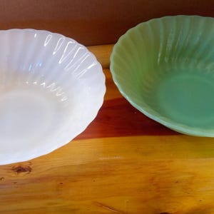 以下が含まれることがあります： 2つのヴィンテージガラスボウル。1つは白、もう1つは薄緑色です。どちらのボウルも外側にスパイラルデザインがあります。ボウルは木製の表面に置かれています。
