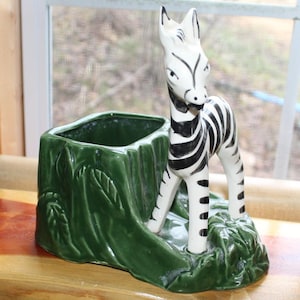 以下が含まれることがあります： 黒い縞模様の白いシマウマと、緑色の切り株型のポットが並んだ陶器のプランター。 プランターは光沢のある仕上げで、インテリアに適しています。