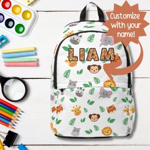 May include: White backpack with a jungle animal pattern, featuring a giraffe, zebra, elephant, monkey, and lion. The name "LIAM" is displayed in brown giraffe print letters. The text "Customize with your name!" is also visible.