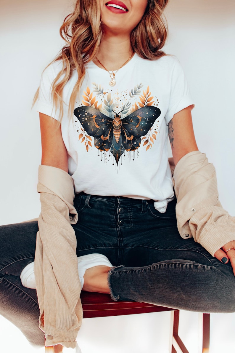 May include: A white t-shirt with a graphic of a dark blue and gold butterfly with gold accents and leaves. The butterfly is surrounded by gold leaves and a white background.