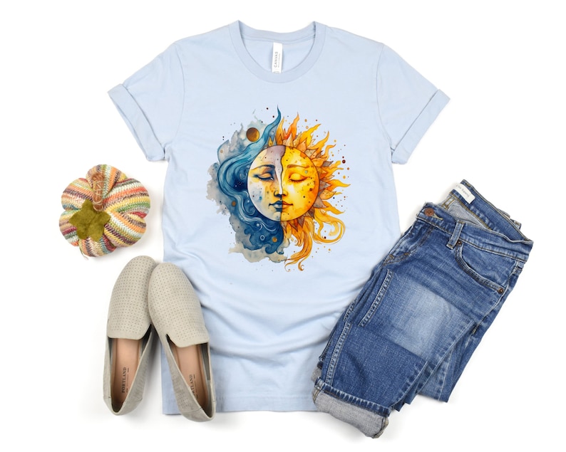 May include: A light blue t-shirt with a watercolor illustration of a sun and moon. The sun is yellow and orange with a face, and the moon is blue and white with a face. The sun and moon are overlapping.