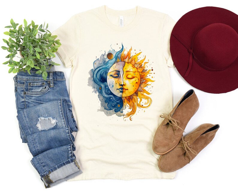 May include: A cream colored t-shirt with a watercolor illustration of a sun and moon with faces. The sun is yellow and the moon is blue. The design is centered on the shirt.
