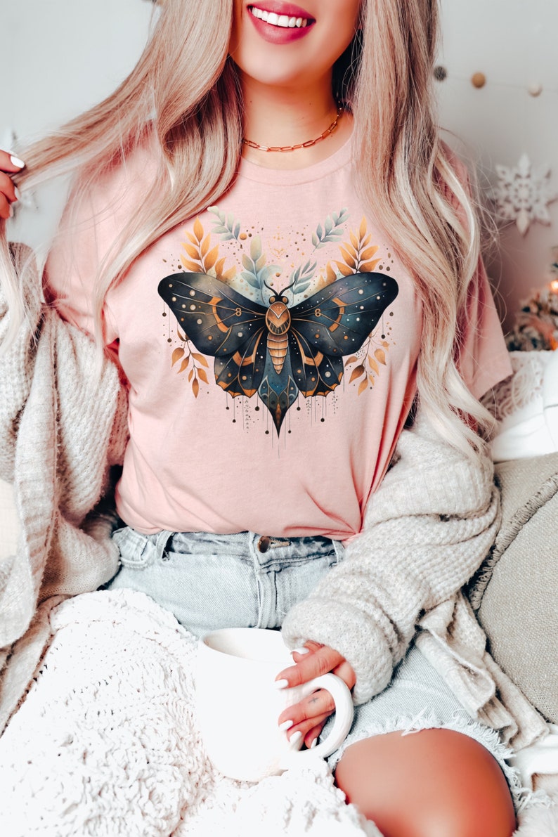 May include: A pink t-shirt with a black and gold butterfly graphic. The butterfly has intricate details and is surrounded by gold leaves.