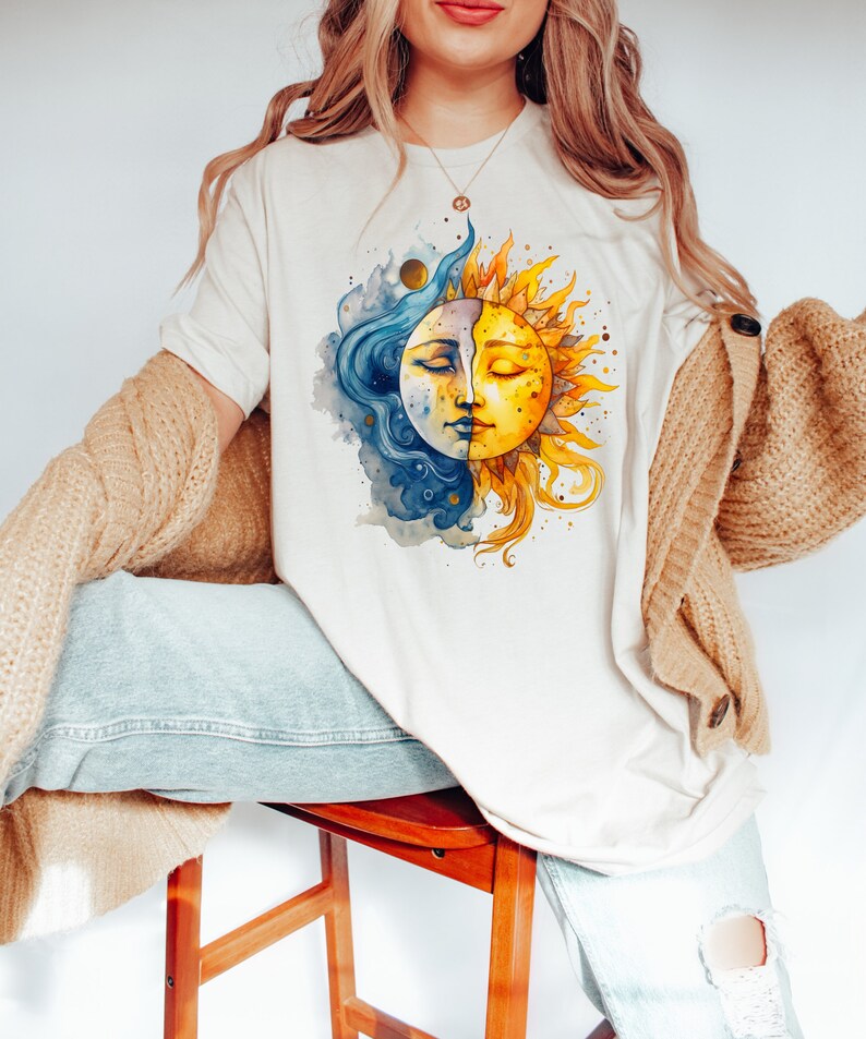 May include: A white t-shirt with a watercolor illustration of a sun and moon with faces. The sun is yellow and the moon is blue.
