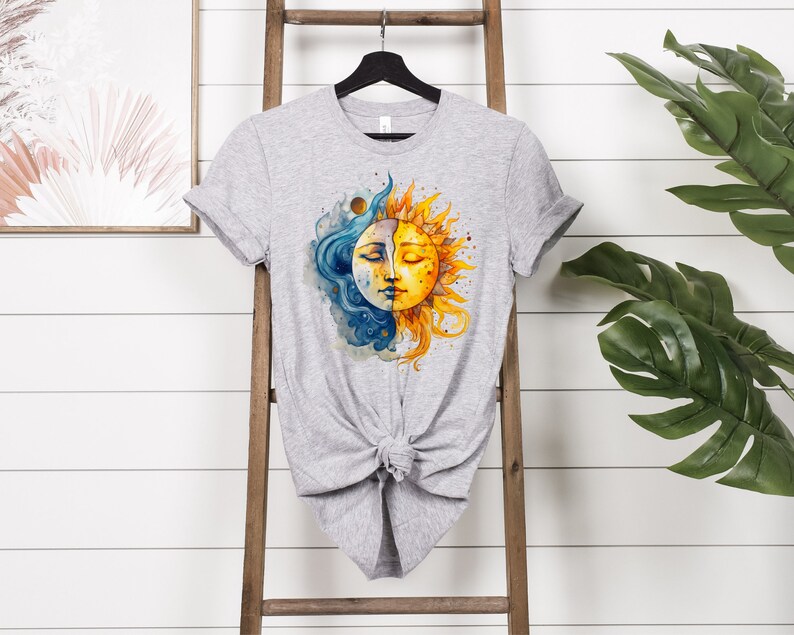 May include: A gray t-shirt with a watercolor design of a sun and moon. The sun is yellow and orange with a smiling face. The moon is blue and white with a face that is half closed eyes. The design is centered on the shirt.