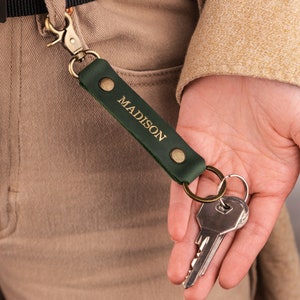 May include: Green leather keychain with a gold metal clasp and a gold metal key ring. The keychain has the name "MADISON" embossed in gold lettering.