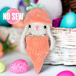 May include: A crocheted carrot-shaped bunny toy with a green top, wrapped in a crocheted orange blanket. The bunny is sitting in a wicker basket with colorful Easter eggs.