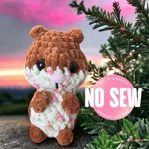 May include: A brown and white crocheted hamster toy with a pink nose and black eyes. The toy is sitting on a rock with a green tree and a pink sunset in the background. The text "NO SEW CROCHET PATTERN" is on a pink circle behind the toy.
