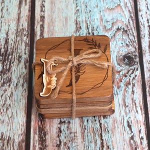 May include: Set of four wooden coasters with a floral design and a letter "J" in the center. The coasters are tied together with twine and a wooden letter "J" charm is attached.