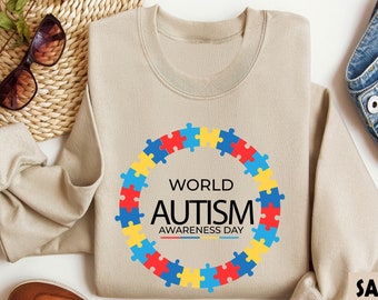 May include: A beige sweatshirt with a colorful puzzle piece design that reads "World Autism Awareness Day".