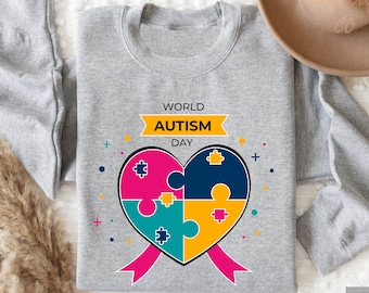 May include: A gray sweatshirt with the text "World Autism Day" and a heart-shaped puzzle piece design. The heart is made up of four puzzle pieces in pink, blue, green, and yellow.