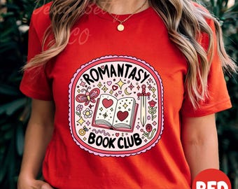 May include: Red t-shirt with a graphic of a book with hearts and a sword, surrounded by stars and flowers. The text "Romantasy Book Club" is written on the book.