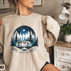 May include: A beige sweatshirt with a graphic of a camper van parked in a forest at night. The text "Home is where you park it." is printed below the graphic.
