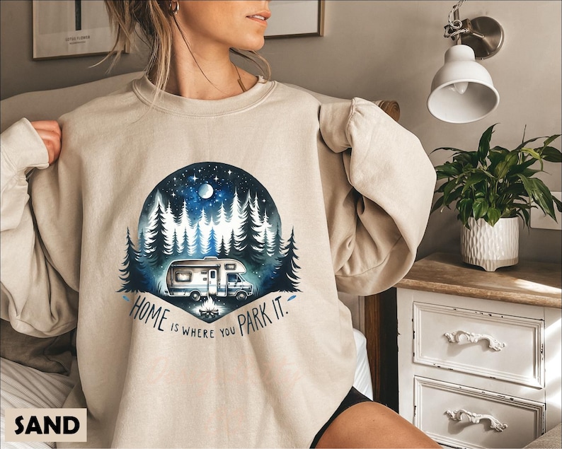 May include: A beige sweatshirt with a graphic of a camper van parked in a forest at night. The text "Home is where you park it." is printed below the graphic.