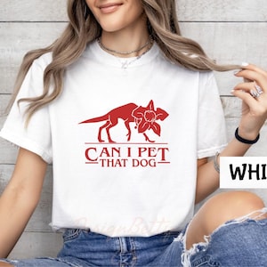 A woman wearing a white t-shirt with a red graphic and text printed on it, posing in front of a white wall.