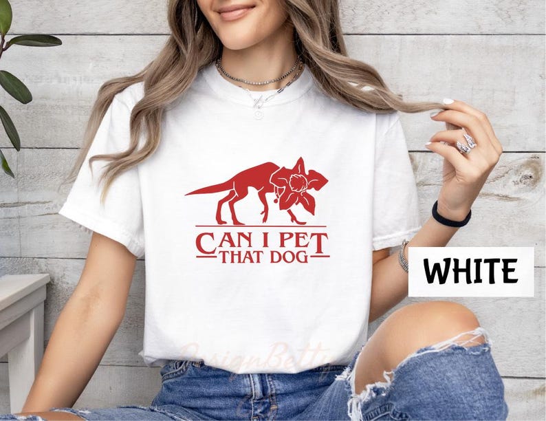A woman wearing a white t-shirt with a red graphic and text printed on it, posing in front of a white wall.