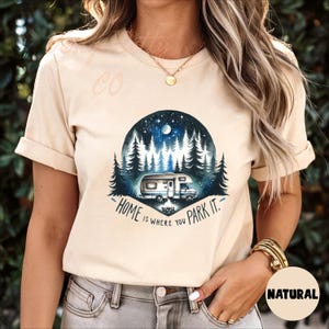 May include: A beige t-shirt with a graphic of a camper van parked in a forest at night. The text "Home is where you park it." is printed below the graphic.