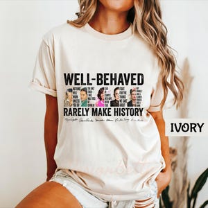 May include: A white t-shirt with the text "WELL-BEHAVED RARELY MAKE HISTORY" and a collage of famous women, including Ruth Bader Ginsburg, Michelle Obama, and Oprah Winfrey. The text "IVORY" is in the bottom right corner.