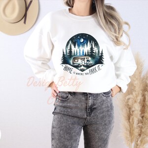 May include: White sweatshirt with a graphic of a camper van in a forest at night. The text "Home is where you park it." is printed on the sweatshirt.