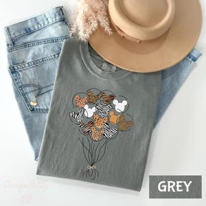 A gray t-shirt with a graphic design of a bunch of balloons in various colors, including yellow, orange, and brown, along with a beige hat and a pair of blue jeans.