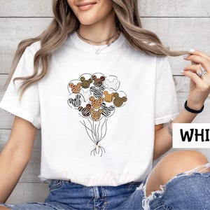A woman wearing a white t-shirt with a graphic of a bunch of balloons and various animal designs, including zebras and leopards.