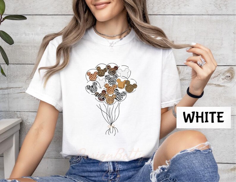 A woman wearing a white t-shirt with a graphic of a bunch of balloons and various animal designs, including zebras and leopards.