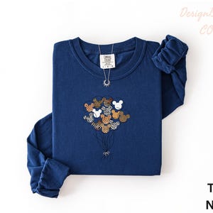 A navy blue long-sleeved shirt with a graphic of a bunch of balloons and a small elephant design on it, along with a necklace.