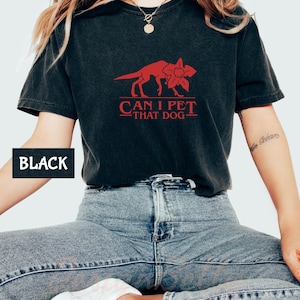 A person wearing a black t-shirt with a red graphic and text, sitting on a chair.