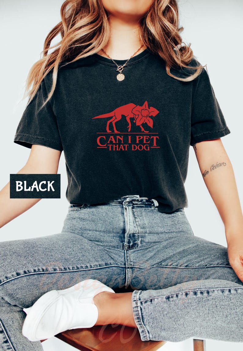 A person wearing a black t-shirt with a red graphic and text, sitting on a chair.