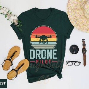 a shirt that says drone pilot next to a hat and sunglasses