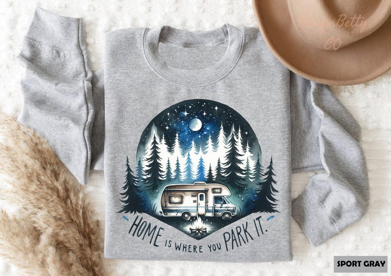 May include: A gray sweatshirt with a watercolor illustration of a camper van parked in a forest at night. The text "Home is where you park it." is printed below the illustration.