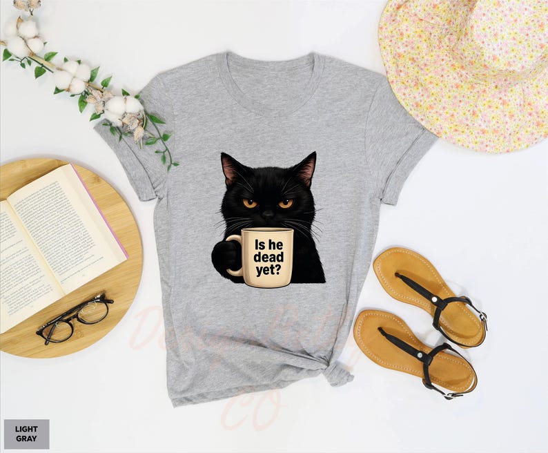 K&ouml;nnte beinhalten: Hellgraues T-Shirt mit einer schwarzen Katze, die eine Kaffeetasse mit der Aufschrift "Is he dead yet?" h&auml;lt.
