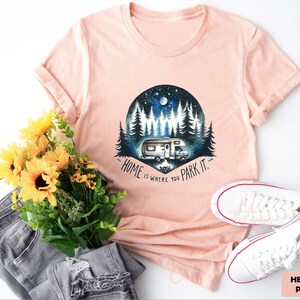 May include: A peach colored t-shirt with a graphic of a camper van parked in a forest with the text "Home is where you park it."