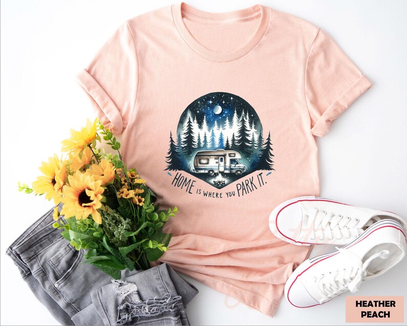 May include: A peach colored t-shirt with a graphic of a camper van parked in a forest with the text "Home is where you park it."