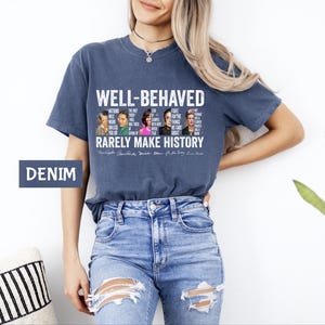 May include: A navy blue t-shirt with a white graphic print that says "Well-Behaved Rarely Make History". The graphic features a collage of famous women and men with quotes about their accomplishments. The shirt is being modeled by a person wearing blue jeans.